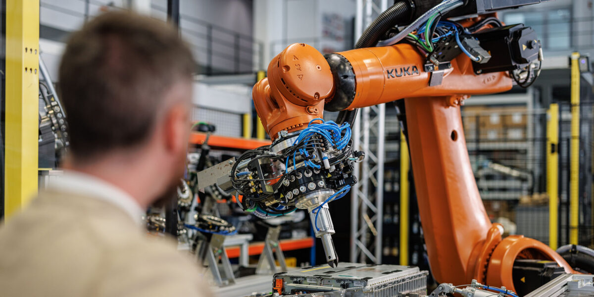 Ein Mitarbeiter des Fraunhofer IPA beobachtet die Arbeitsschritte: Die effiziente, roboterunterstützte Batteriedemontage sorgt dafür, dass sich das Batterierecycling auch wirtschaftlich lohnt. Foto: Kuka 