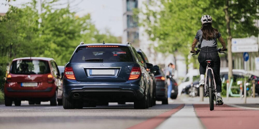 Mensch auf dem Fahrrad und auf dem Radweg fahrend während die Autos daneben unterwegs sind.