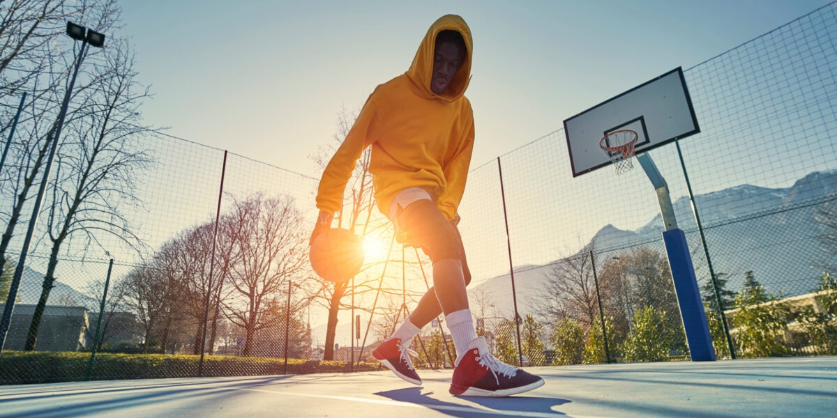 Athletic black man training basketball outdoors.