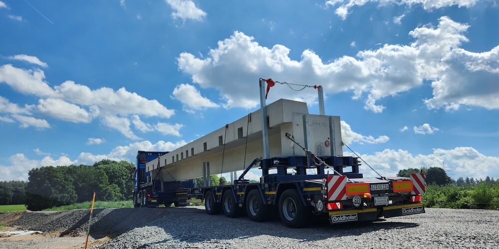 Vorgefertigte Brückenbauteile werden auf einem Tieflader zur Baustelle transportiert.