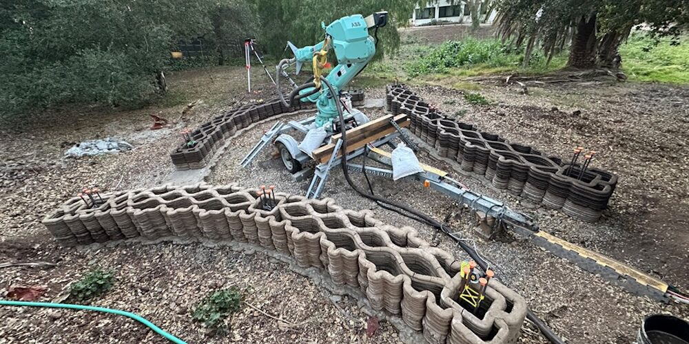 Das Bild zeigt eine Forschungsbaustelle, auf der mithilfe eines 3D-Druckers Formen aus Lehm hergestellt werden, in denen anschließend Beton gegossen werden kann.