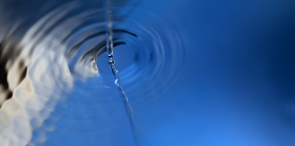 Ein Wasserstrahl verursacht Ringe auf einer Wasseroberfläche