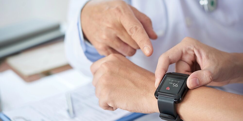 Smartwatch am Arm zeigt der Patient seinem Arzt die Daten, die auf dem Display ablesbar sind.